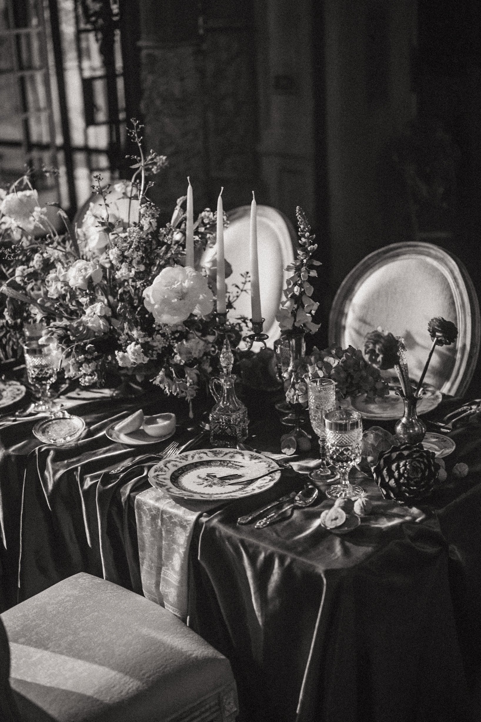 Elegant dining table set with floral arrangements, candlesticks, glassware, and fine china, in a dimly lit room with vintage decor.